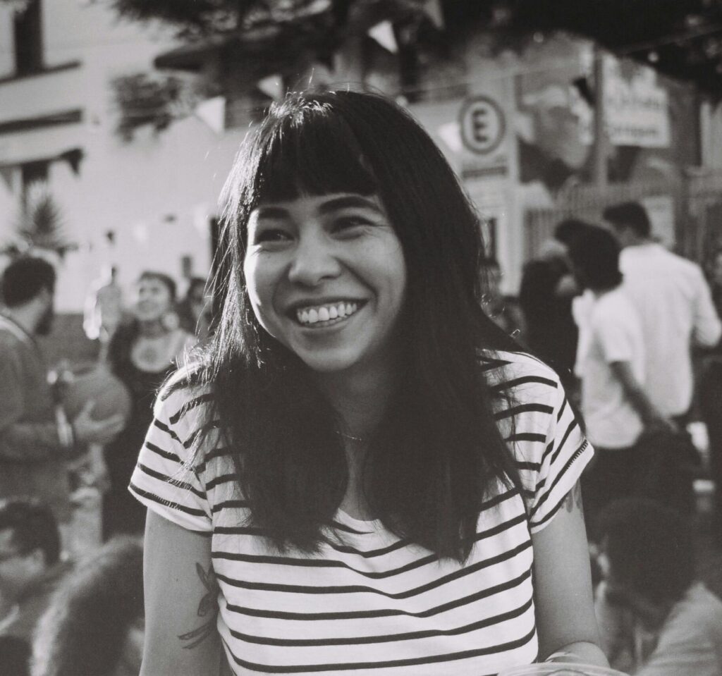 Smiling woman in striped shirt at an outdoor gathering, captured in black and white film.