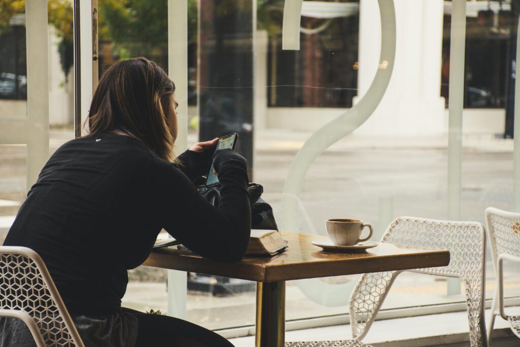 A woman enjoys coffee while using her smartphone at a cozy cafe table.