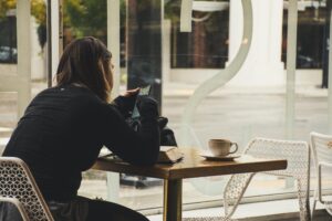 A woman enjoys coffee while using her smartphone at a cozy cafe table.