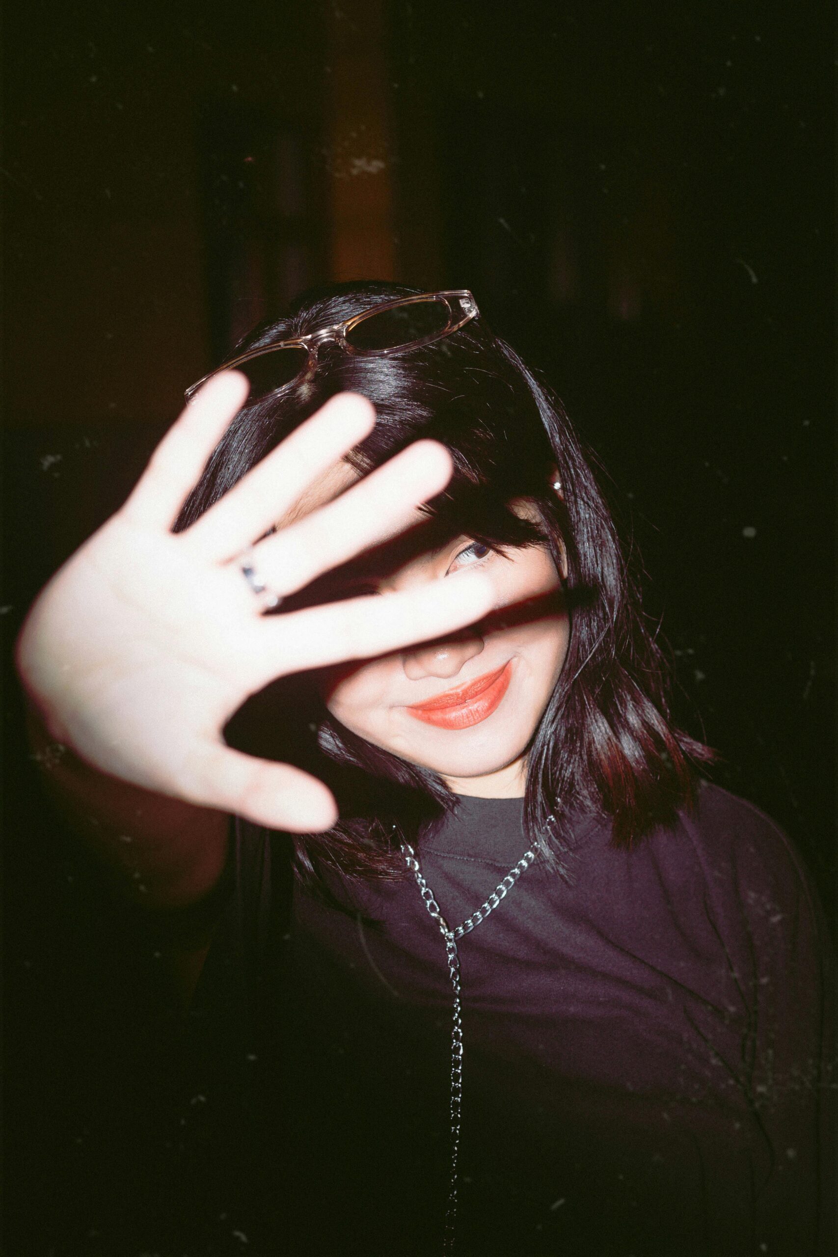 Young woman smiling with her hand covering her face, wearing sunglasses.